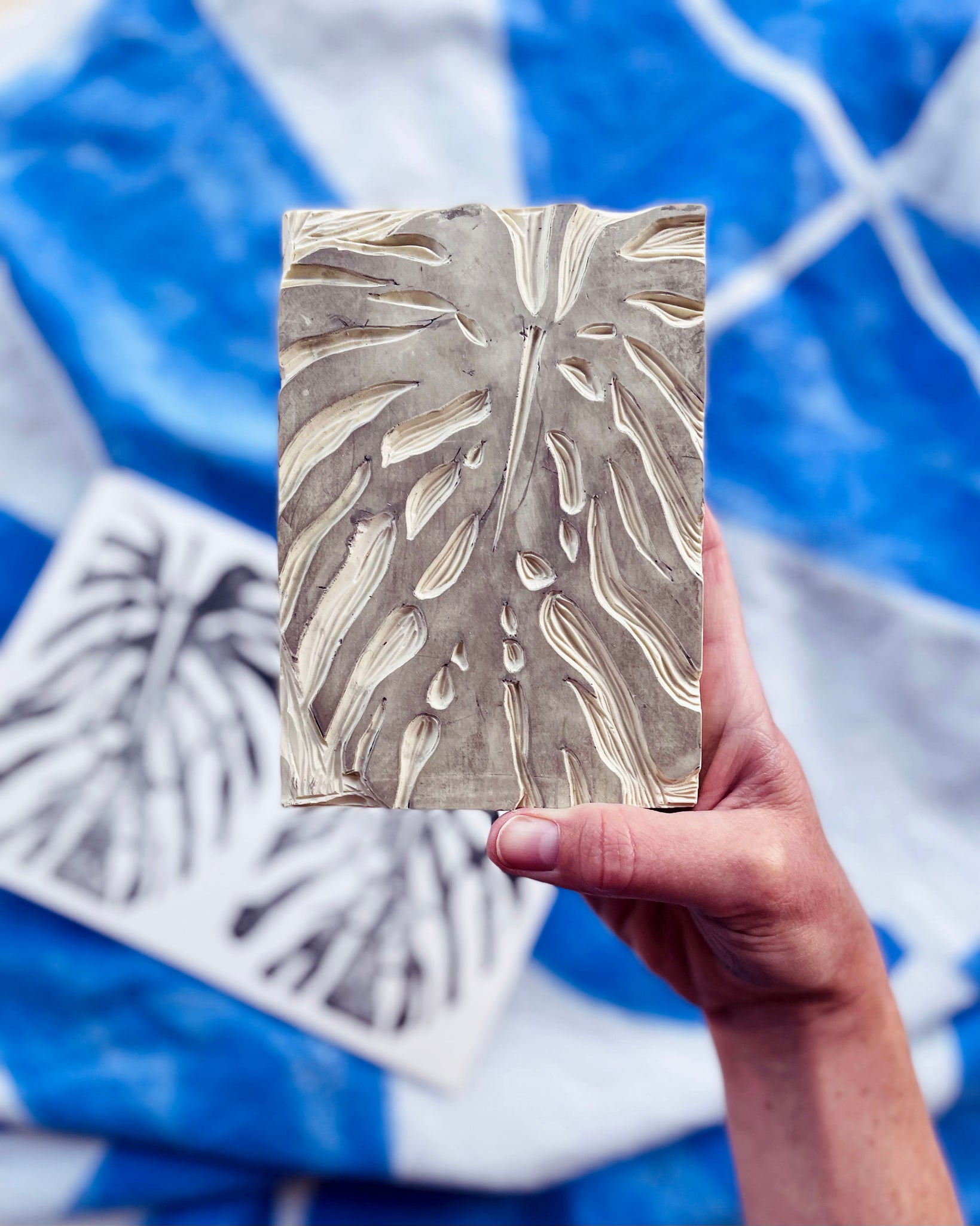 A hand holds the pattern of a block print block.