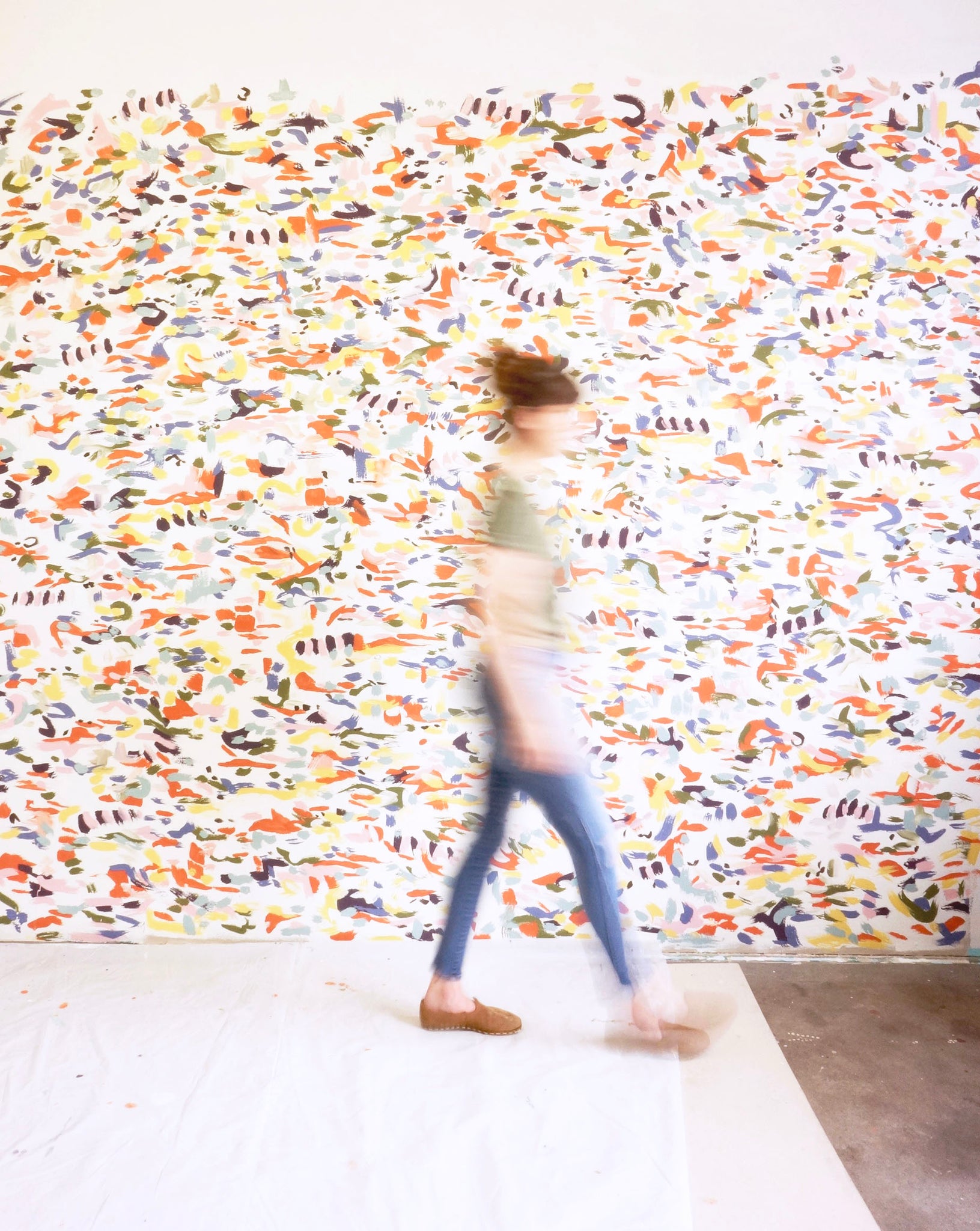 Meg walks by a patterned wall in a studio space.